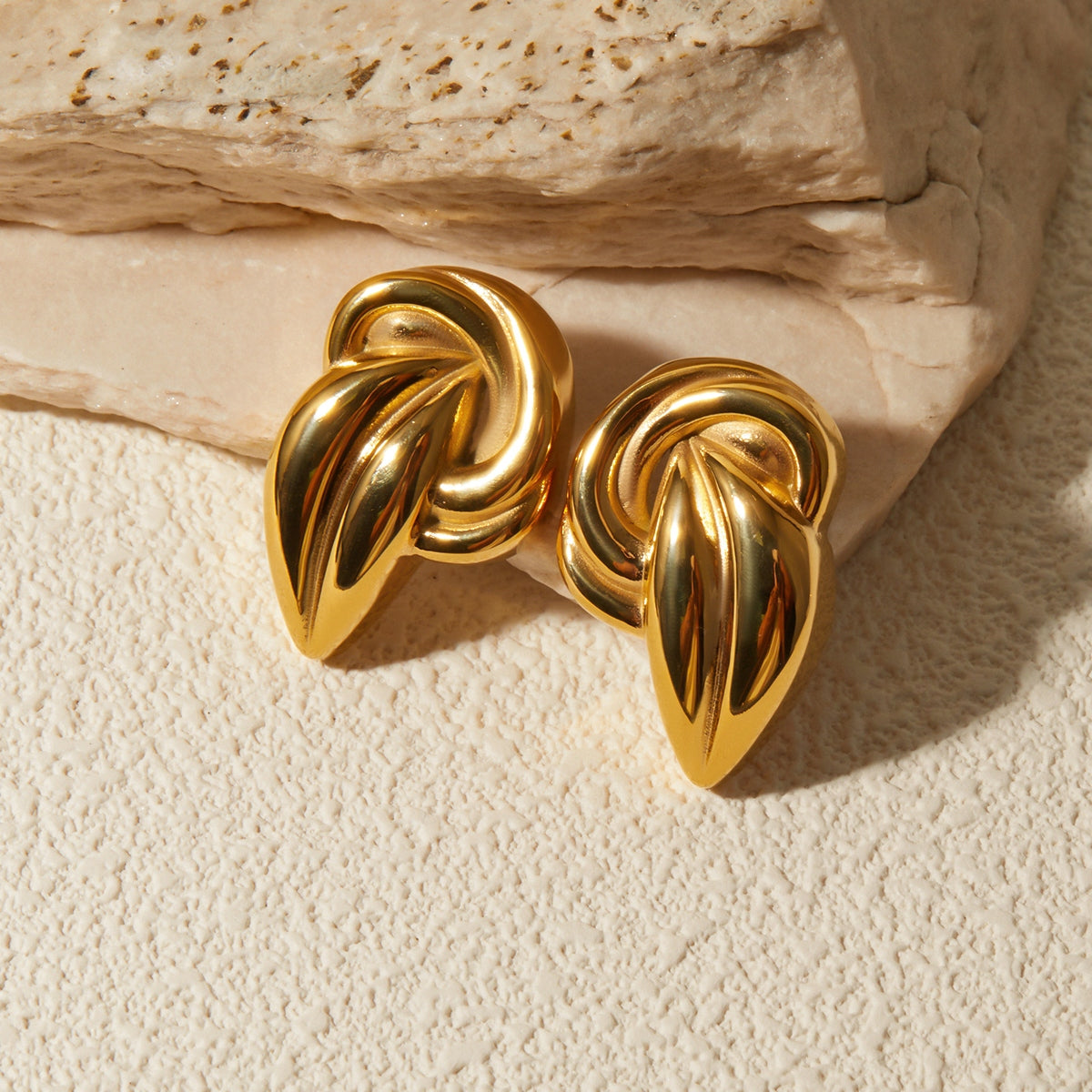 "A close-up view of earring an 18K Gold-Plated Stud Earrings. The earring features an intricate design with a twisted knot shape, adding a bold and elegant touch to the overall appearance."