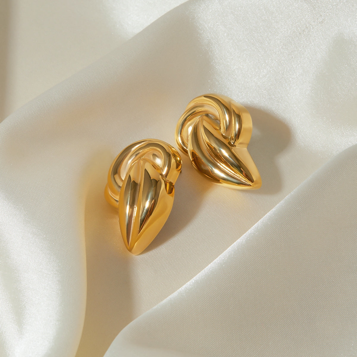 "A close-up view of earring an 18K Gold-Plated Stud Earring. The earring features an intricate design with a twisted knot shape, adding a bold and elegant touch to the overall appearance."