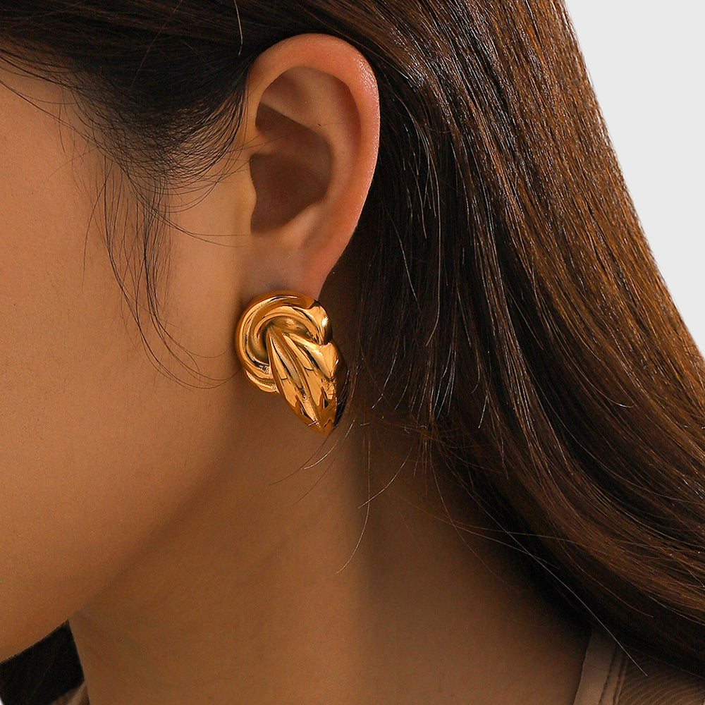 "A close-up view of a woman's ear wearing an 18K Gold-Plated Stud Earrings. The earring features an intricate design with a twisted knot shape, adding a bold and elegant touch to the overall appearance. 18K Gold-Plated Stud Earrings.."